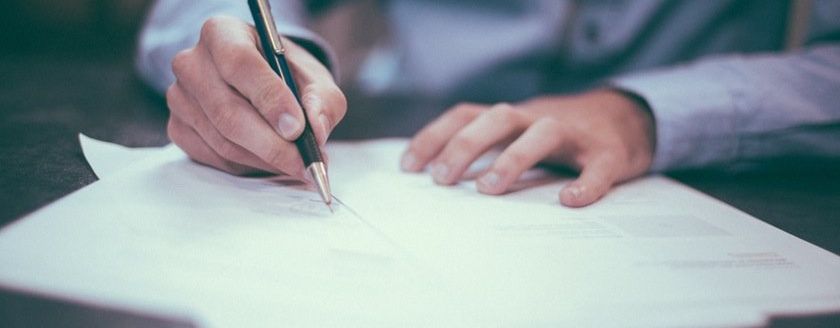 A pair of hands holding a pen while signing professional documents