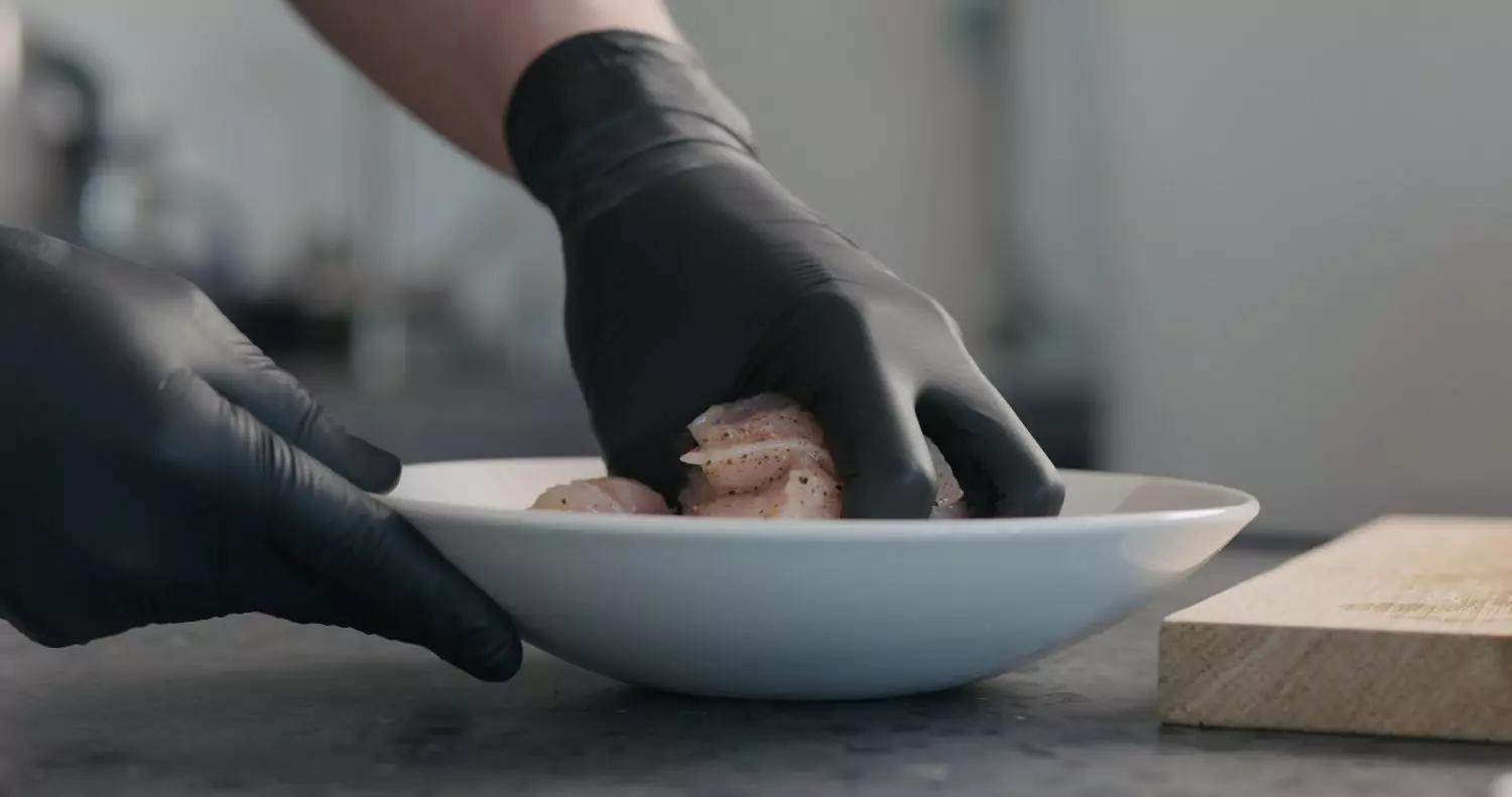 Black disposable gloves handling raw chicken in a kitchen food prep setting