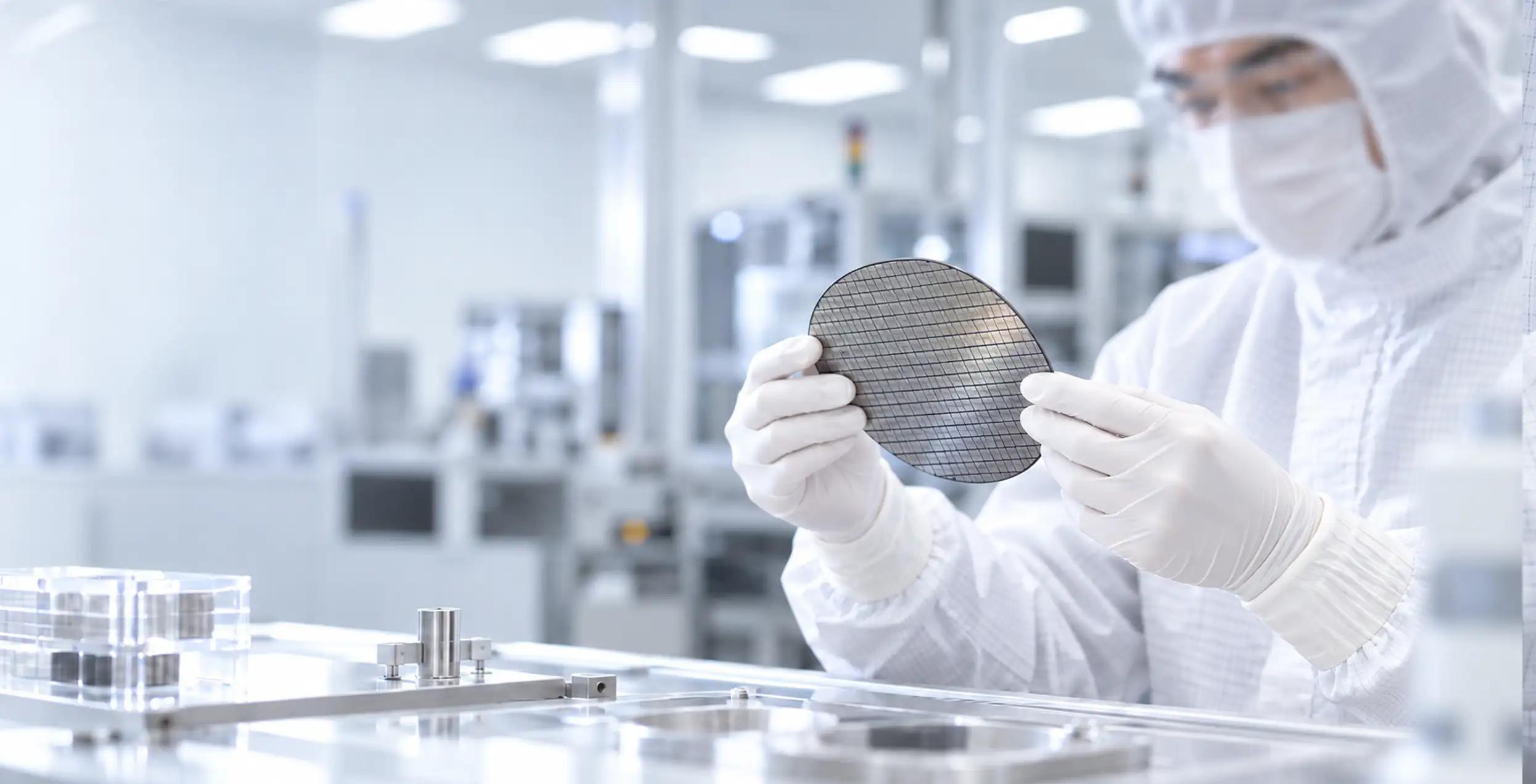 Cleanroom technician wearing white nitrile gloves while inspecting a semiconductor wafer in a controlled environment