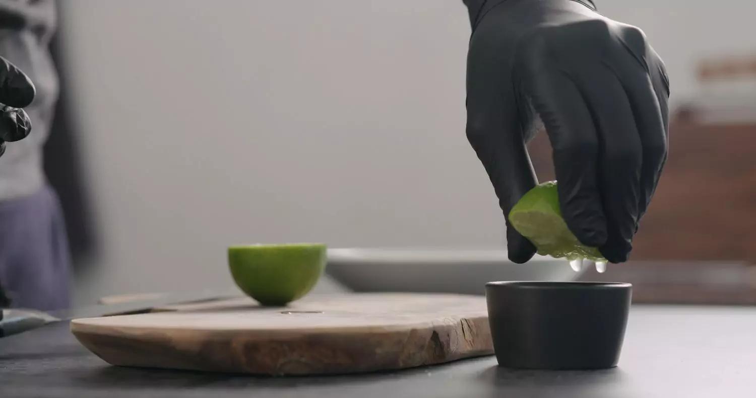 Black disposable gloves squeezing lime for food preparation