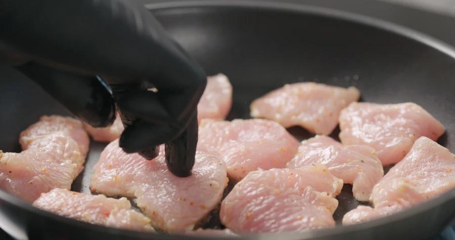 Black Disposable Gloves used for handling raw chicken in a frying pan