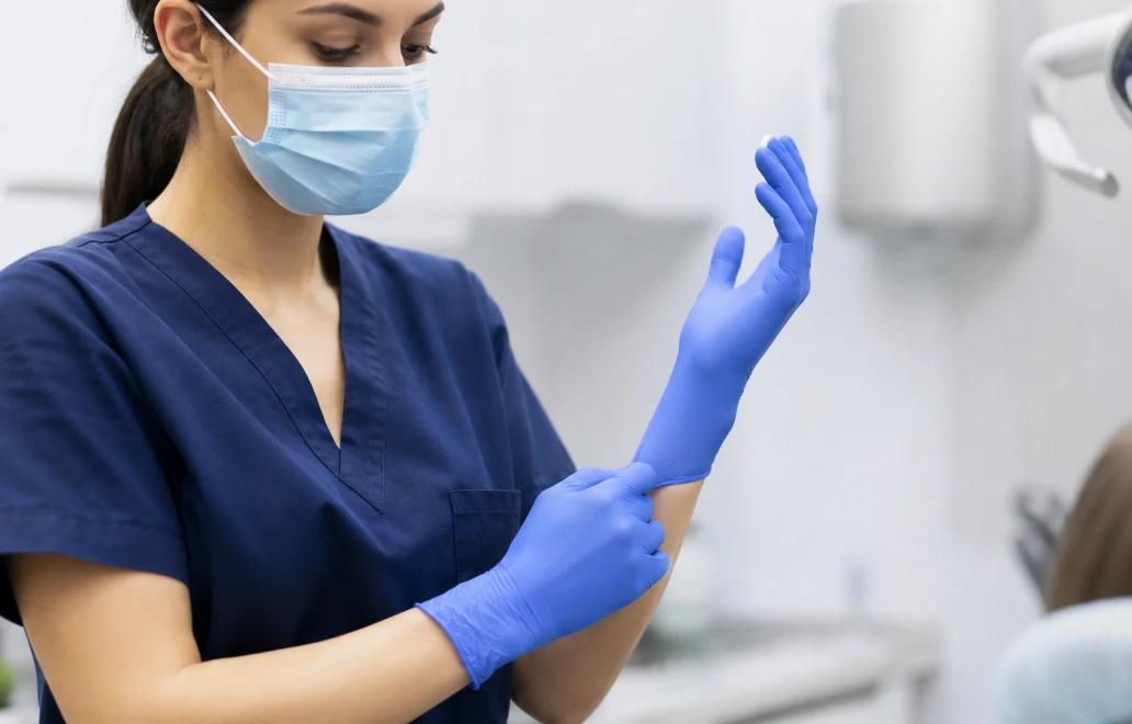 Medical staff putting on blue nitrile gloves in a clinical setting, preparing for patient care