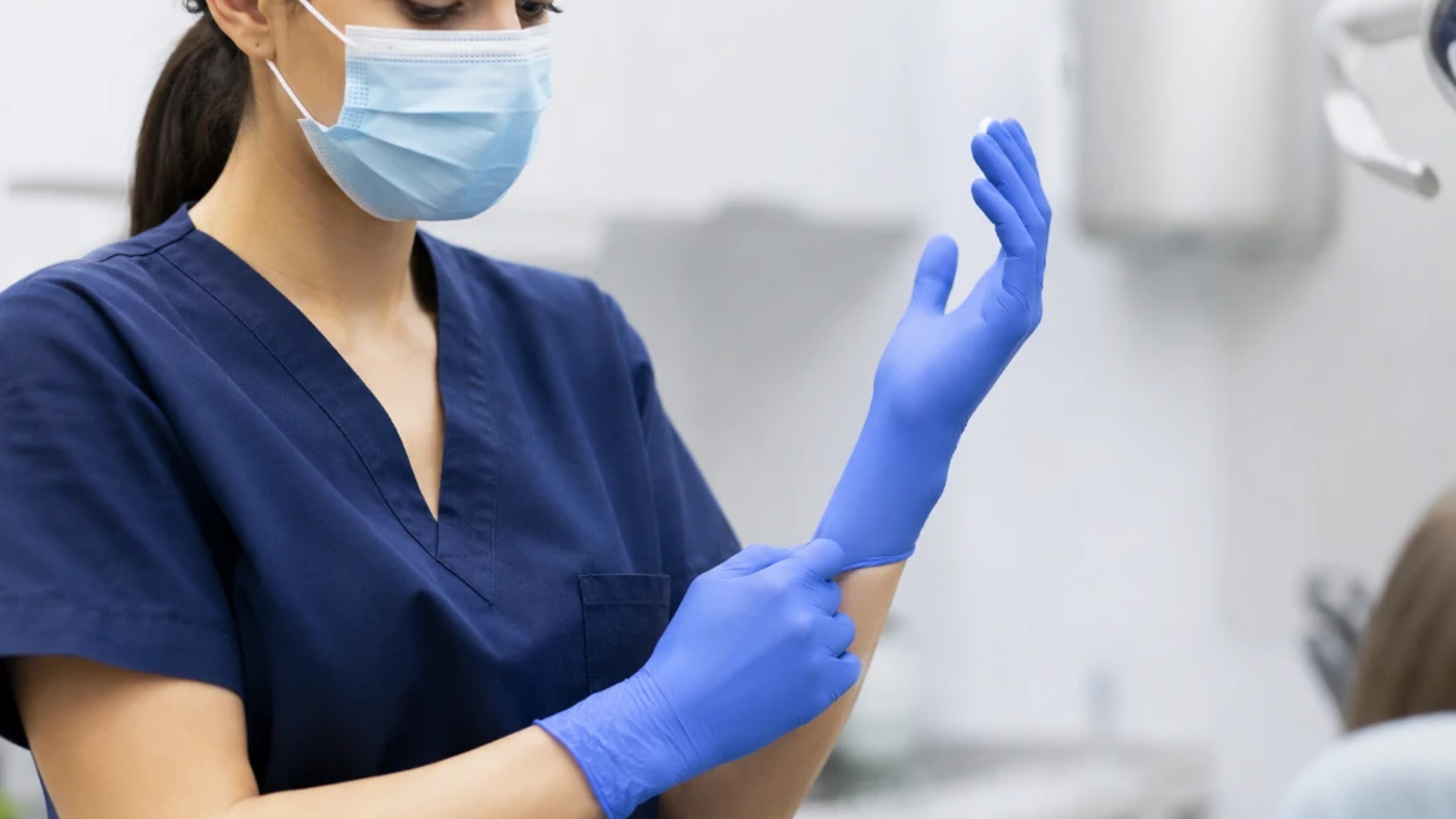 Medical staff putting on blue nitrile gloves in a clinical setting, preparing for patient care