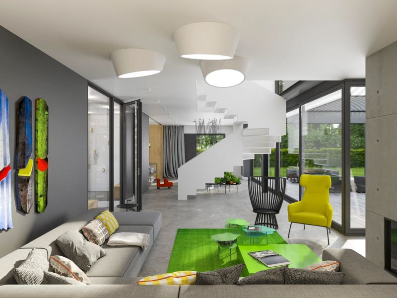 Nowoczesny salon z narożną szarą sofą, zieloną wyspą, żółtym fotelem i oświetleniem sufitowym. Ściana TV w czerni, schody, dużo światła naturalnego, design minimalistyczny.