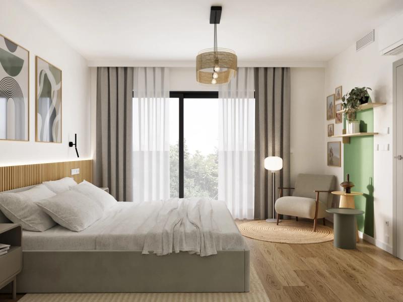 Widok od okna. Szare zasłony z białym firankiem. Zielony stolik obok fotela, szarozielony obok łóżka — kolory powtarzają się, ale nie jednolicie.