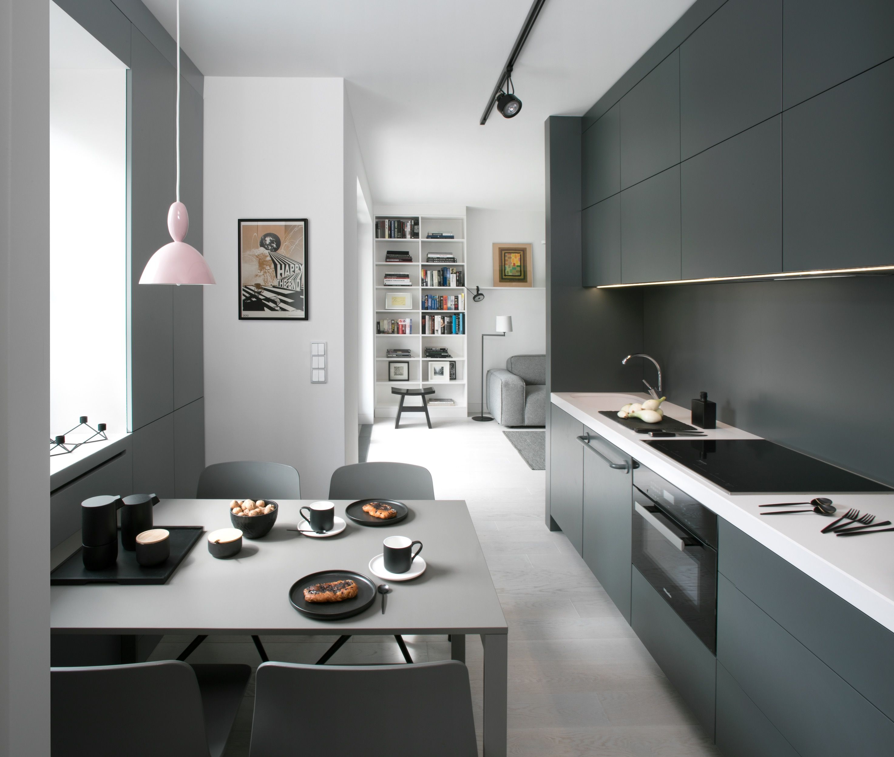 Nowoczesna kuchnia z szarą zabudową, białym blatem, wyspą i jadalnią. Minimalistyczne fronty kuchenne, eleganckie oświetlenie i funkcjonalny layout