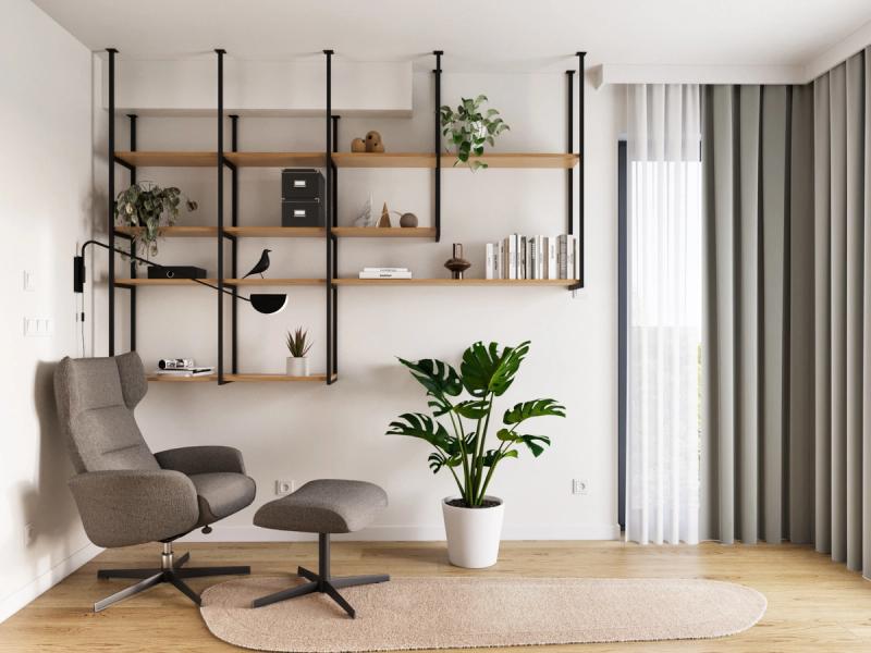 Fotel do czytania i podnóżek. Szarozielone zasłony od podłogi do sufitu zmiękczają ścianę z oknem. Na regale: książki, pudełka, rośliny — wszystko na wyciągnięcie ręki.