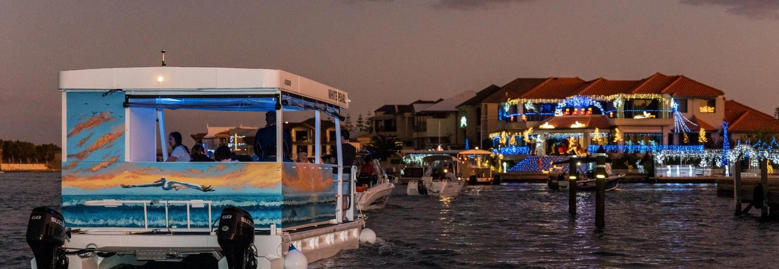 The White Pearl under way at dusk with a full moon overhead, a canal home lit up across the water behind it