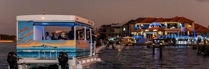 The White Pearl under way at dusk with a full moon overhead, a canal home lit up across the water behind it