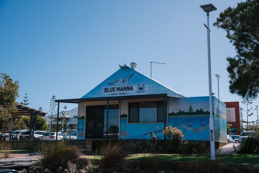 The Blue Manna Boat Hire office, a pale blue building with a painted estuary mural along one wall and its name across the gable