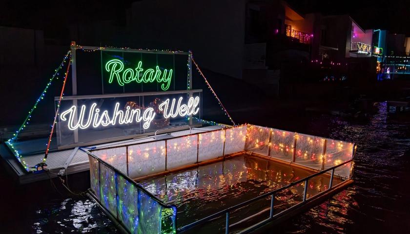 A floating pontoon in the canals strung with fairy lights, carrying neon signs reading Rotary and Wishing Well