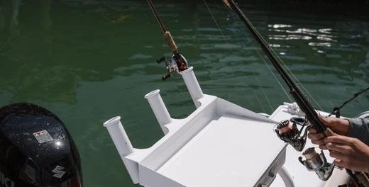 Rod holders and a white bait board on the back of a hire fishing boat, with someone holding a rod over the water