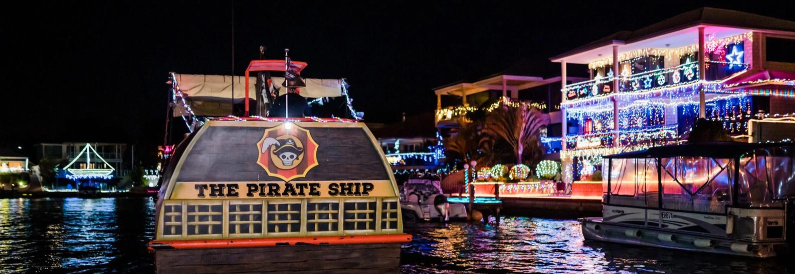 The stern of the Pirate Ship Mandurah passing canal homes covered in Christmas lights after dark