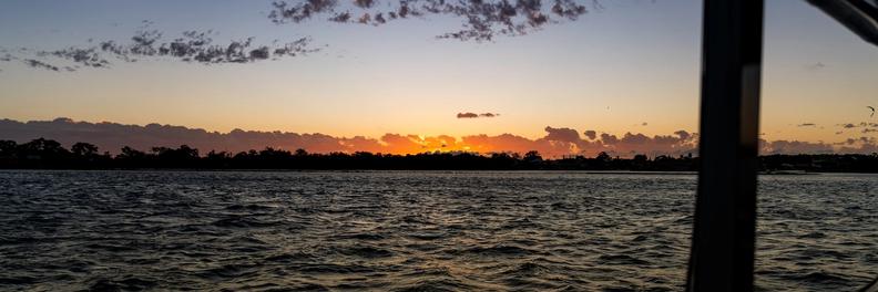 Sunset over the estuary and low treeline, seen through a cabin window onboard a vessel