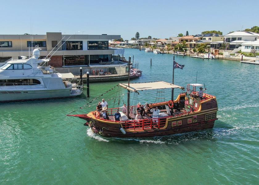 The Pirate Ship passing moored boats in the Mandurah canals, a costumed crew member on the stern deck