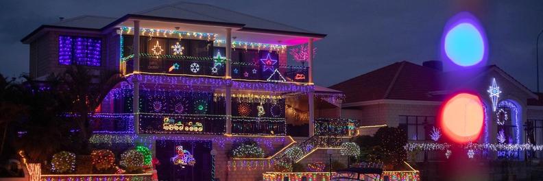 A two-storey canal home lit from roof to jetty in coloured Christmas lights, seen from the water