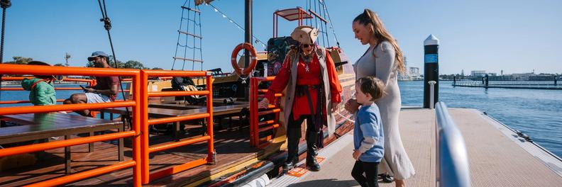A costumed crew member welcomes a woman and young child aboard down the gangway at the Mandurah jetty