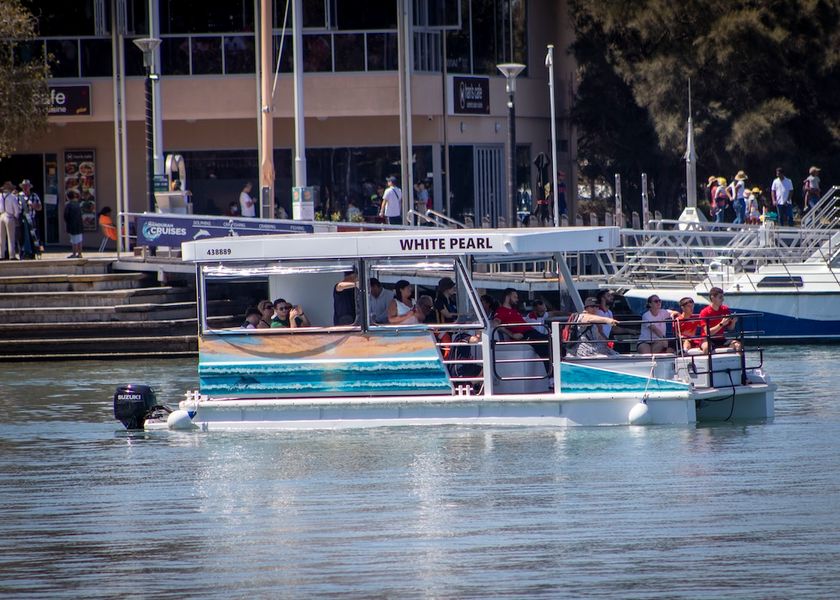 The White Pearl, a white pontoon boat with an open upper deck, cruising past the Mandurah waterfront with passengers aboard