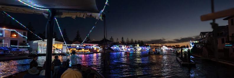 Passengers under the ship's canopy looking down a canal lined with lit homes at last light