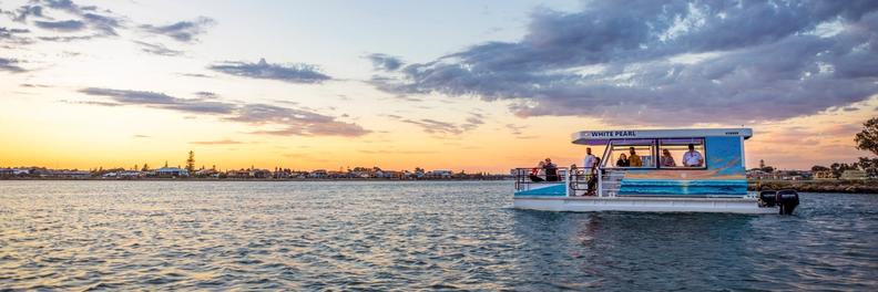 The White Pearl on open water at sunset, passengers on deck against an orange and blue sky