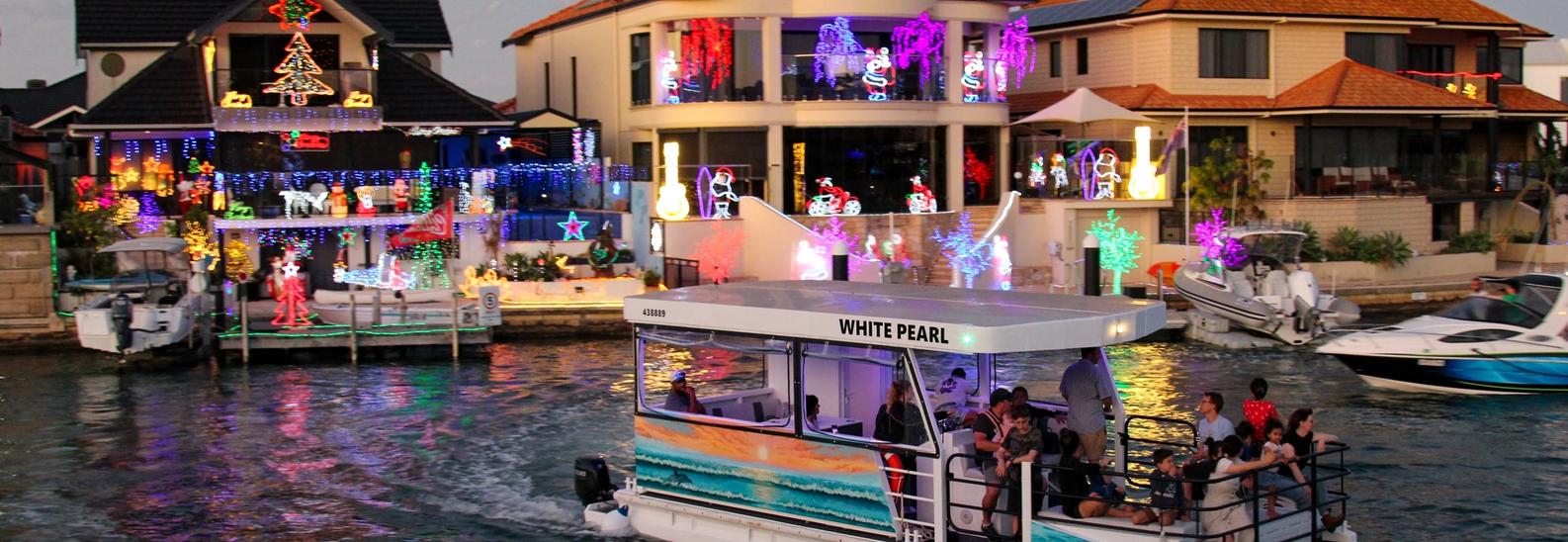 The White Pearl passing a row of canal homes covered in Christmas lights, passengers watching from the open rear deck