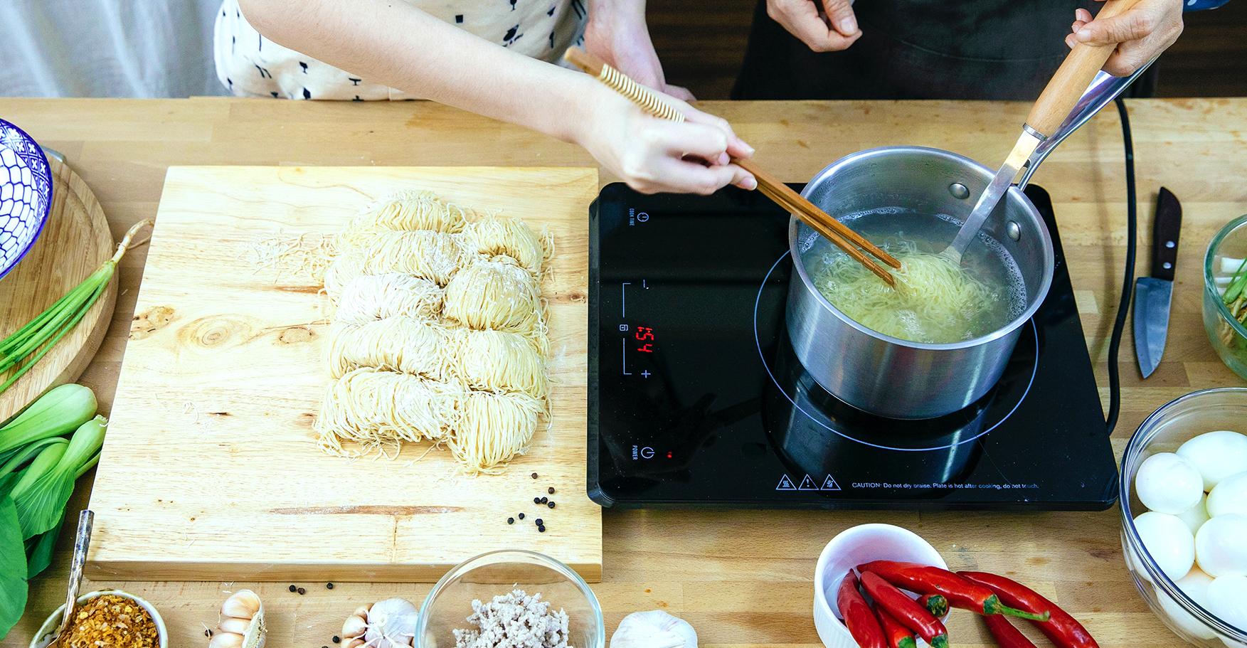 Two women cooking noodles on an induction cooktop