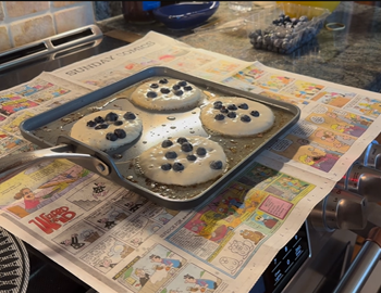 Blueberry pancakes cooking on an induction stove using newspaper as a splashguard
