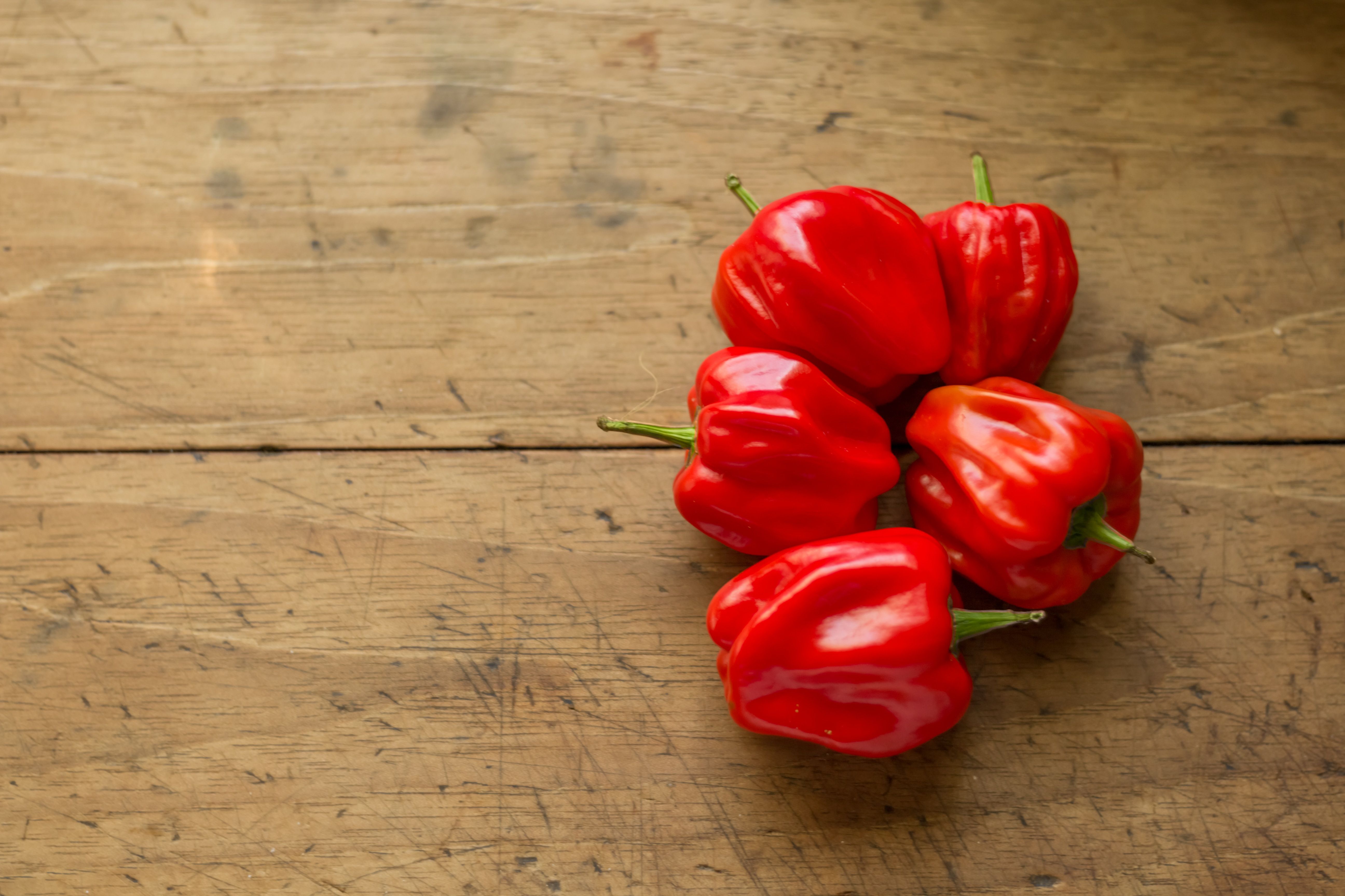 Five red peppers on a wooden surface
