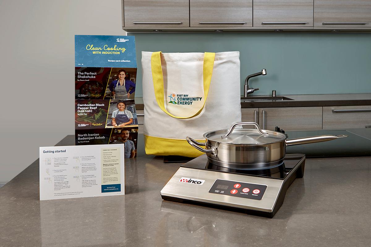 induction cooktop with a stainless steel pan, tote bag and print materials displayed on a kitchen counter