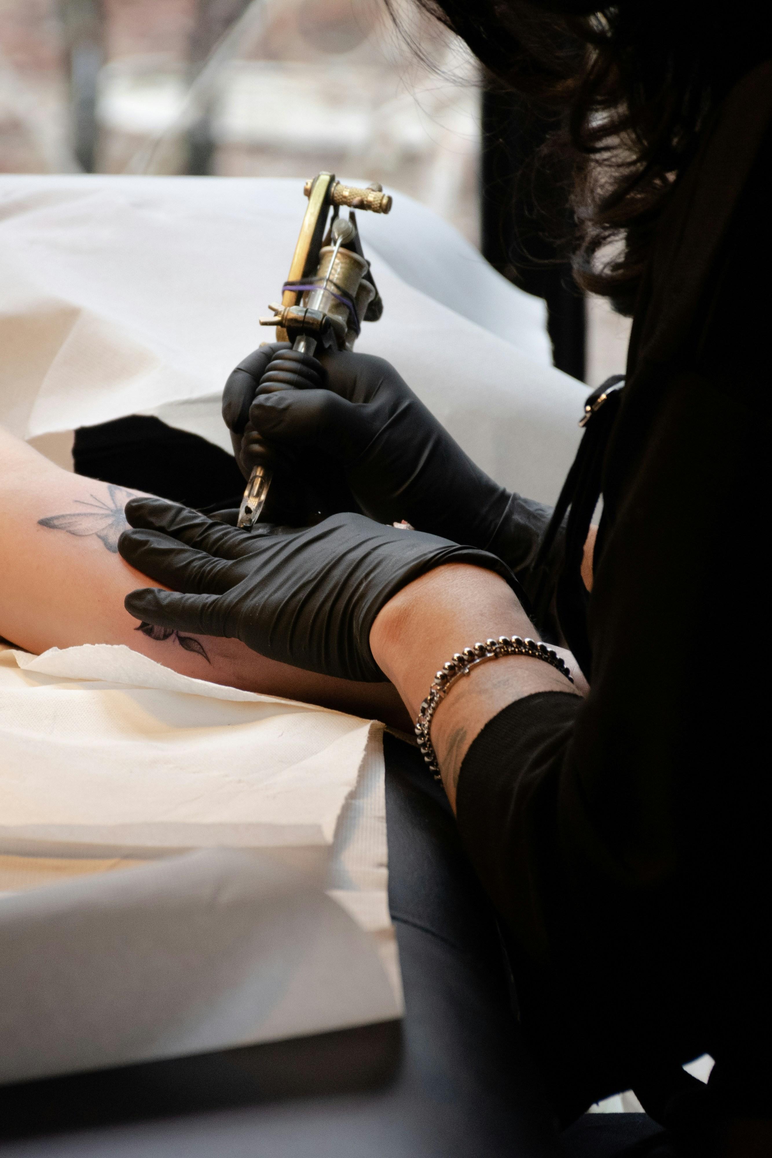 Artist holding a brass coil tattoo machine over a client's arm