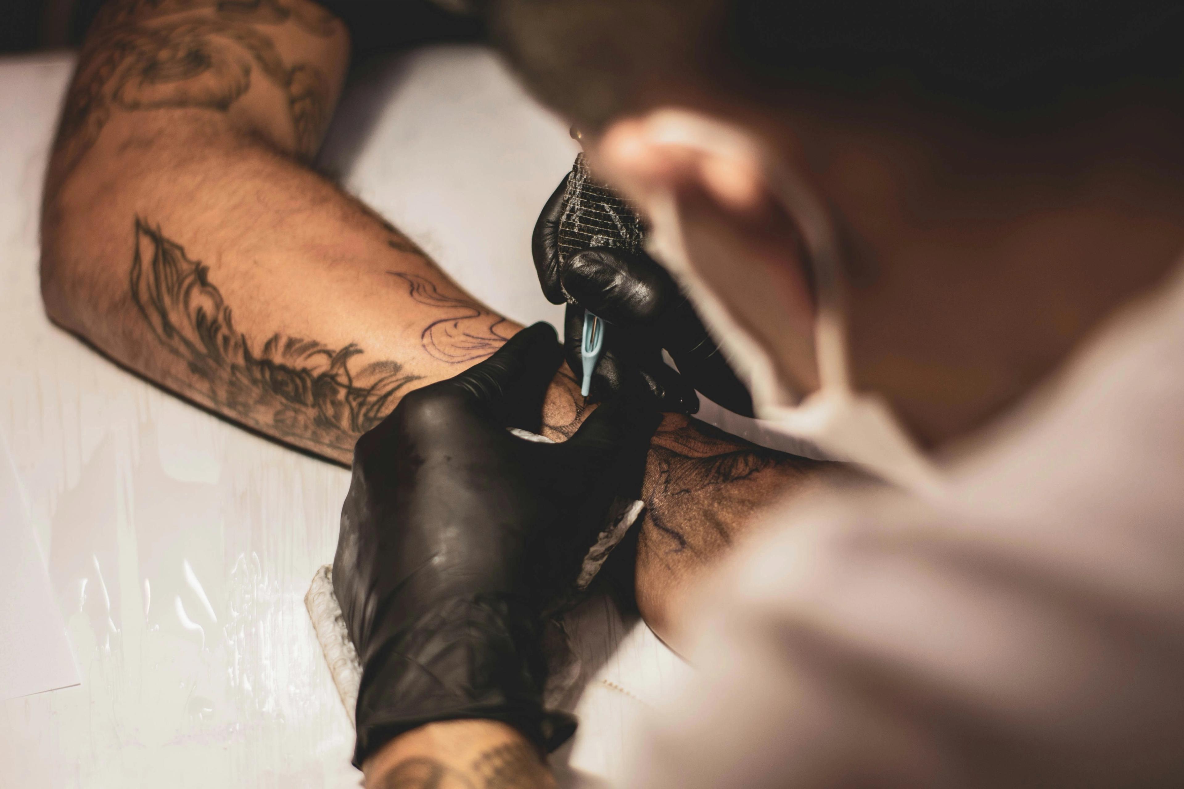 Tattoo artist in black gloves working on a client's forearm