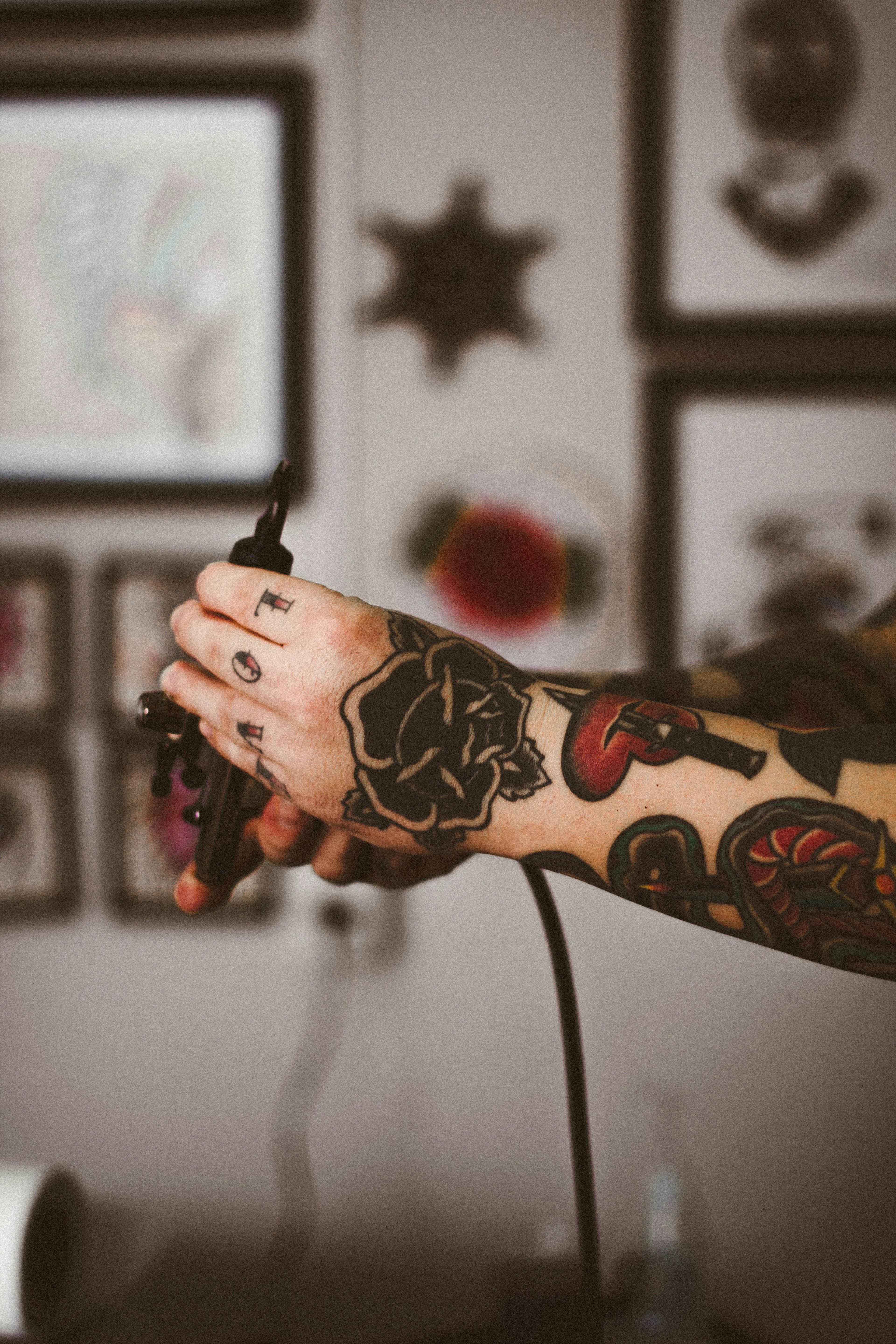 Tattooed arm holding a machine in front of a wall of framed flash art