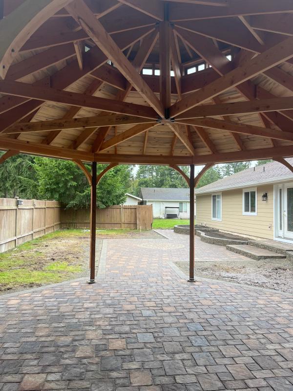 The inside view of a beautiful hardwood gazebo with a pavestone hardscape walkway leading out into the backyard.