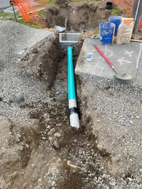 A new drain and pipe exposed in a trench before being covered.