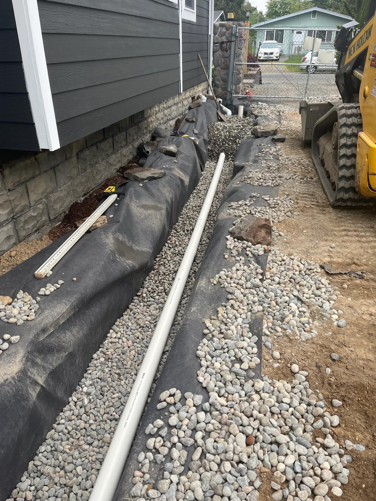 A new drain pipe sitting on a gravel bed beside a house.