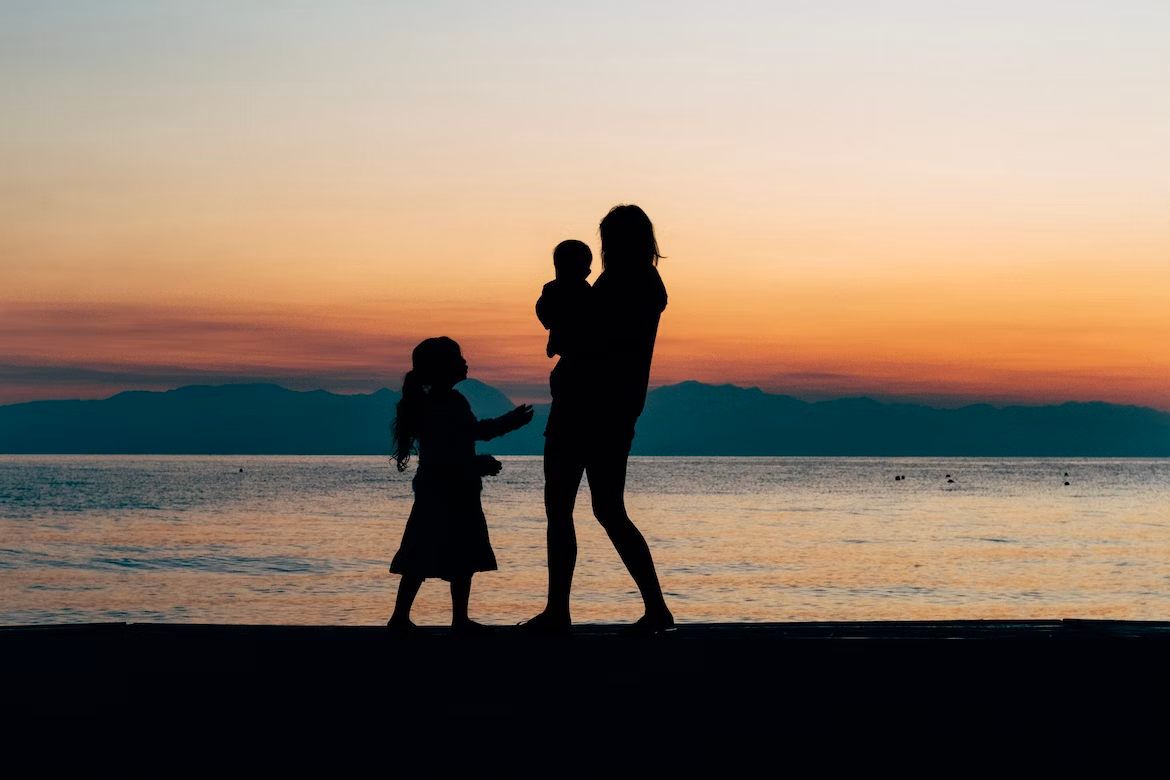 family of three standing together at the beach at sunset