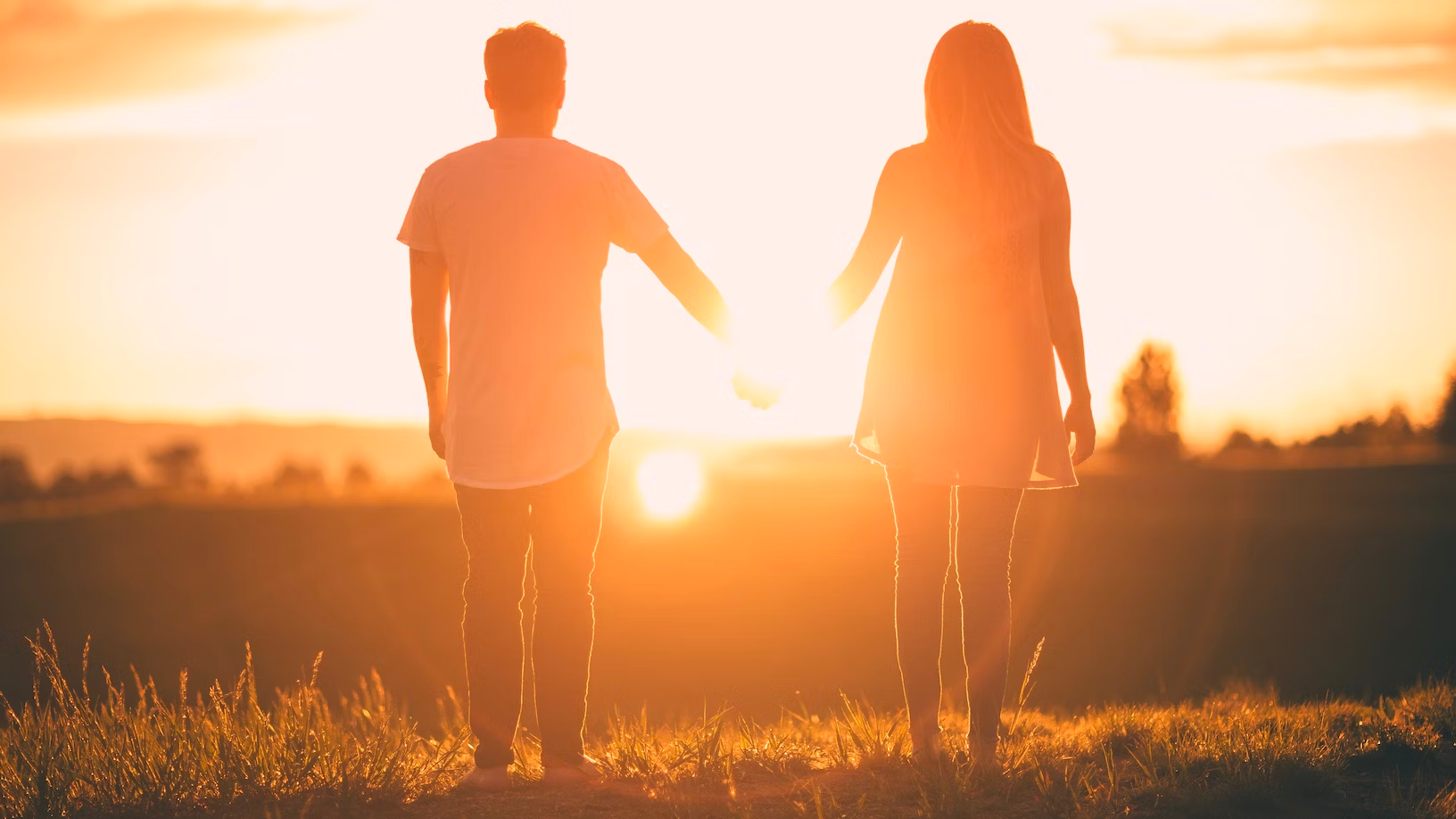 couple standing on a hill holding hands at sunset