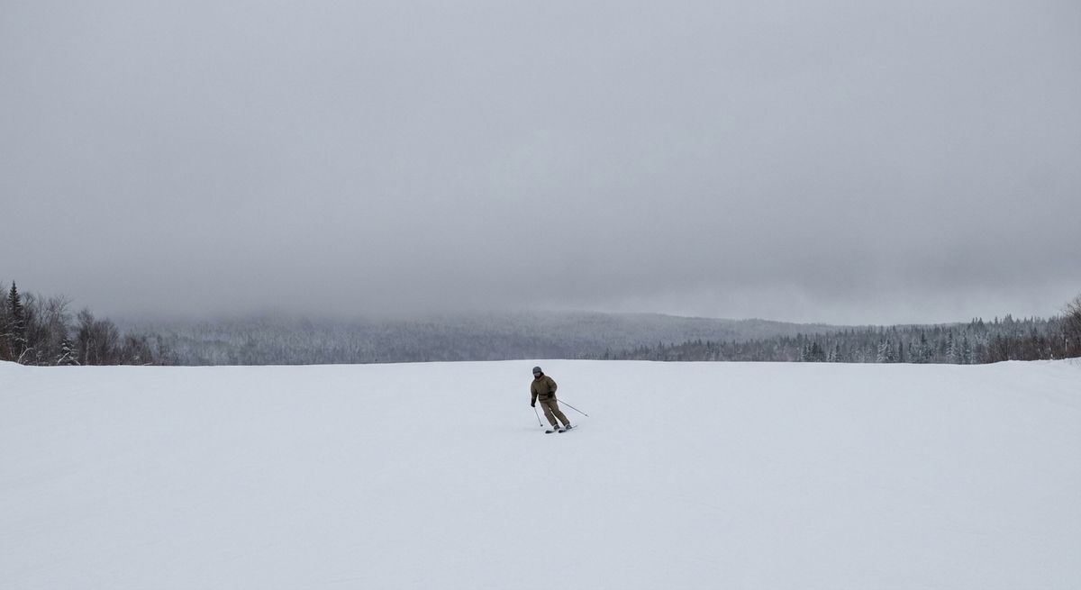A skier making turns on an open groomed run on a grey winter morning, seen from a distance