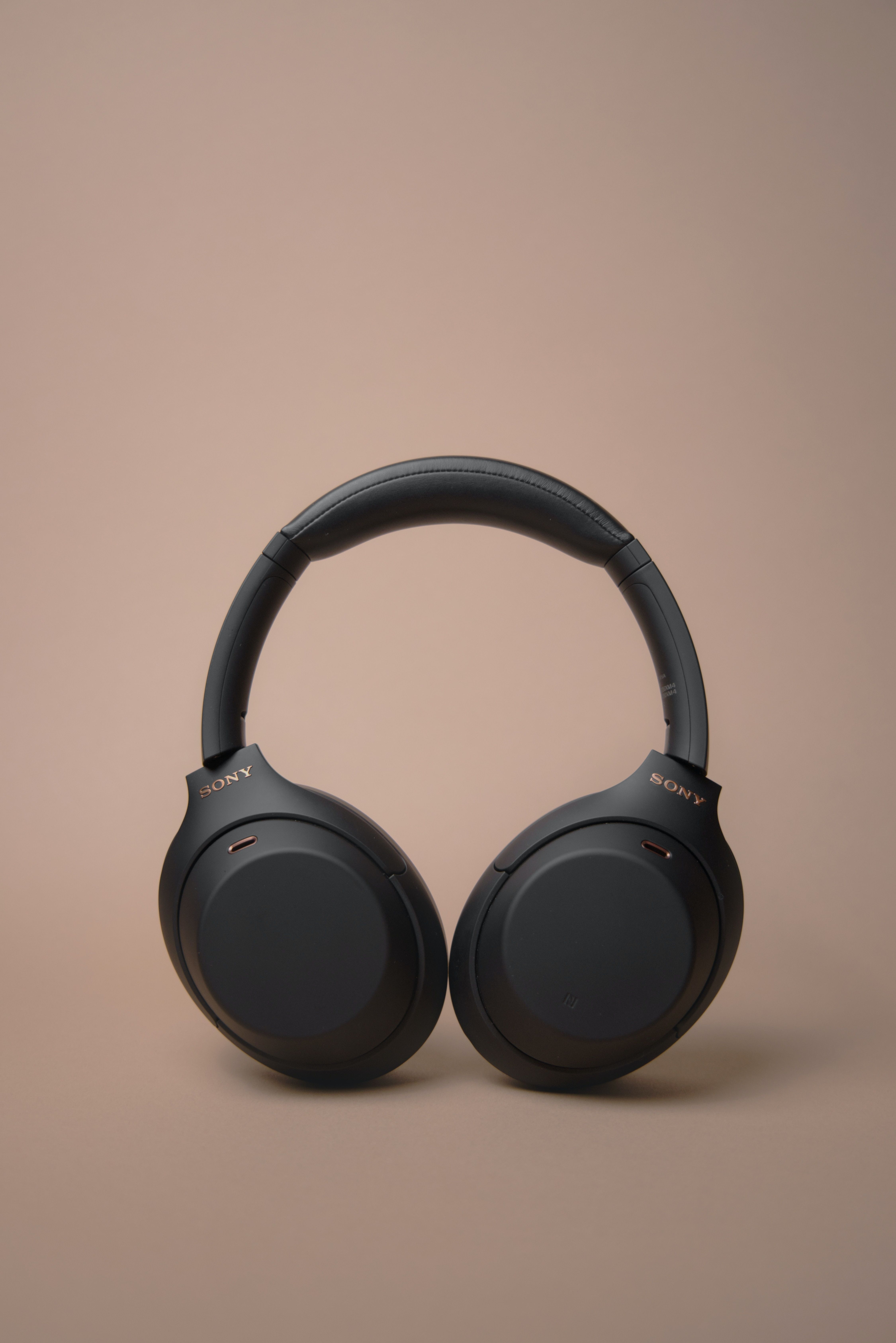 Dark grey wireless headphones against a peach background