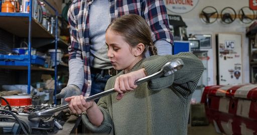Father and daughter bond while fixing a car in a workshop.