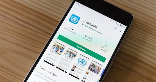 Mobile phone on wooden table showing installation screen for WHO Info app from World Health Organization.