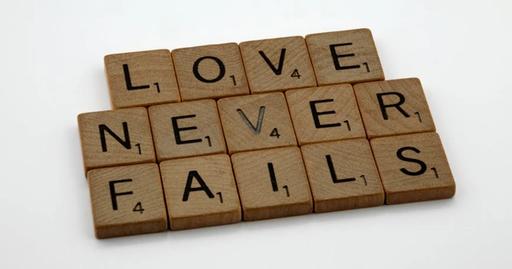 Wooden Scrabble tiles spelling out 'Love Never Fails' on a white background.