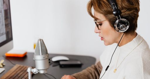 Woman with headphones speaking into a microphone in a modern home studio.