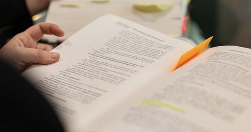 A close-up of hands holding books with highlighted text and notes, symbolizing learning and study.