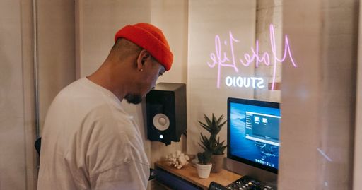 A man wearing a red knit cap works in a recording studio with a computer and audio equipment.