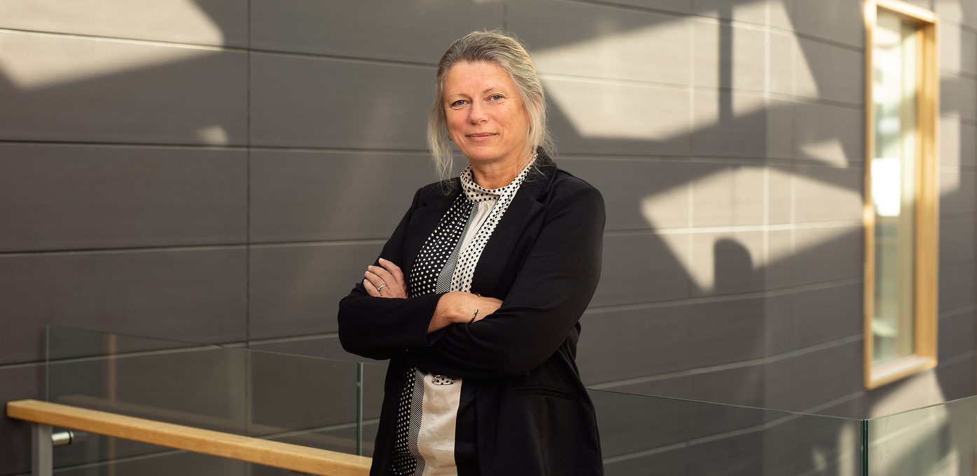Fagdirektør for organisasjon og personale står i eit modernistisk bygg. Ho har armane kryssa og ser rett i kamera.