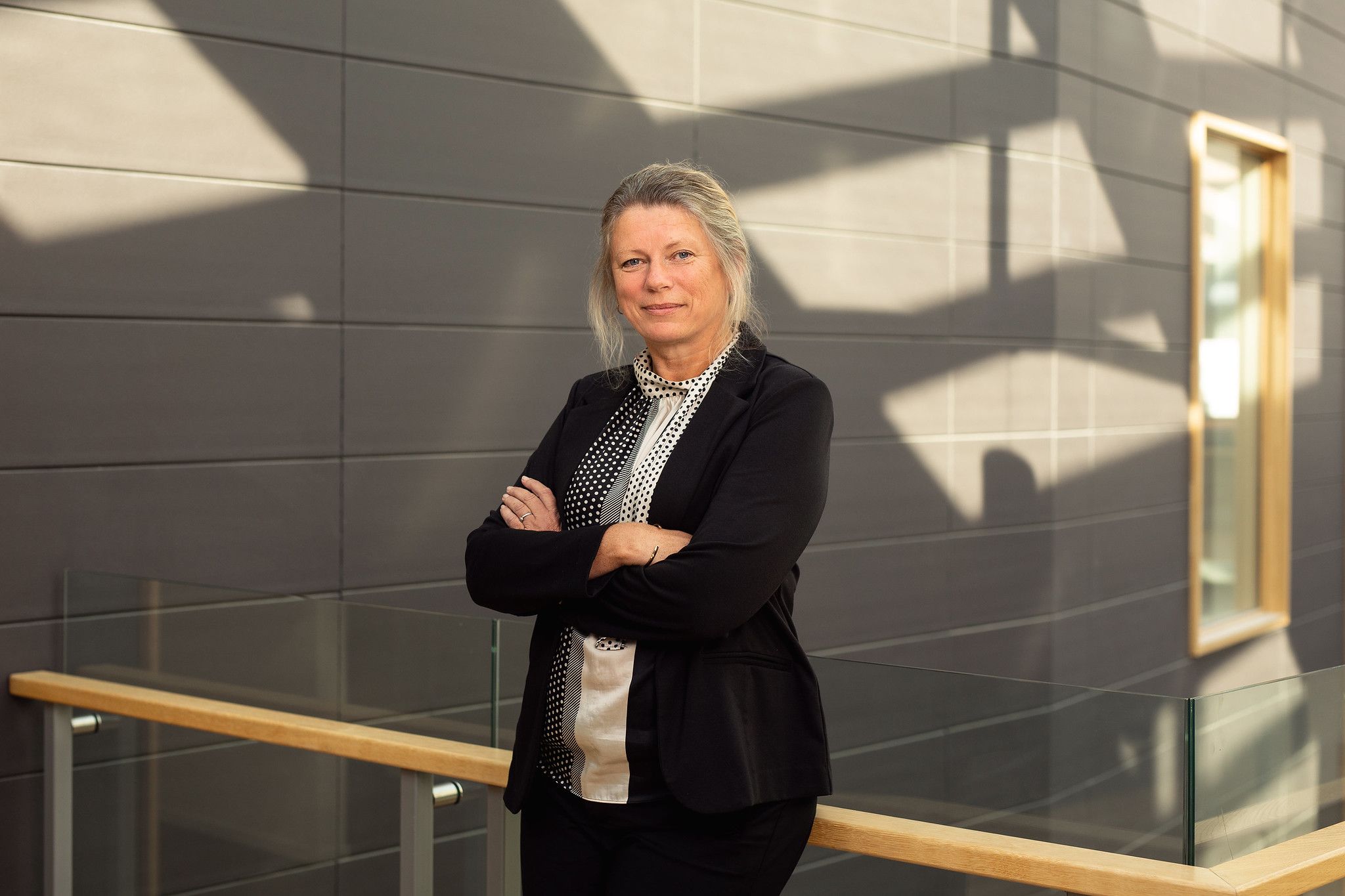 Fagdirektør for organisasjon og personale står i eit modernistisk bygg. Ho har armane kryssa og ser rett i kamera. 