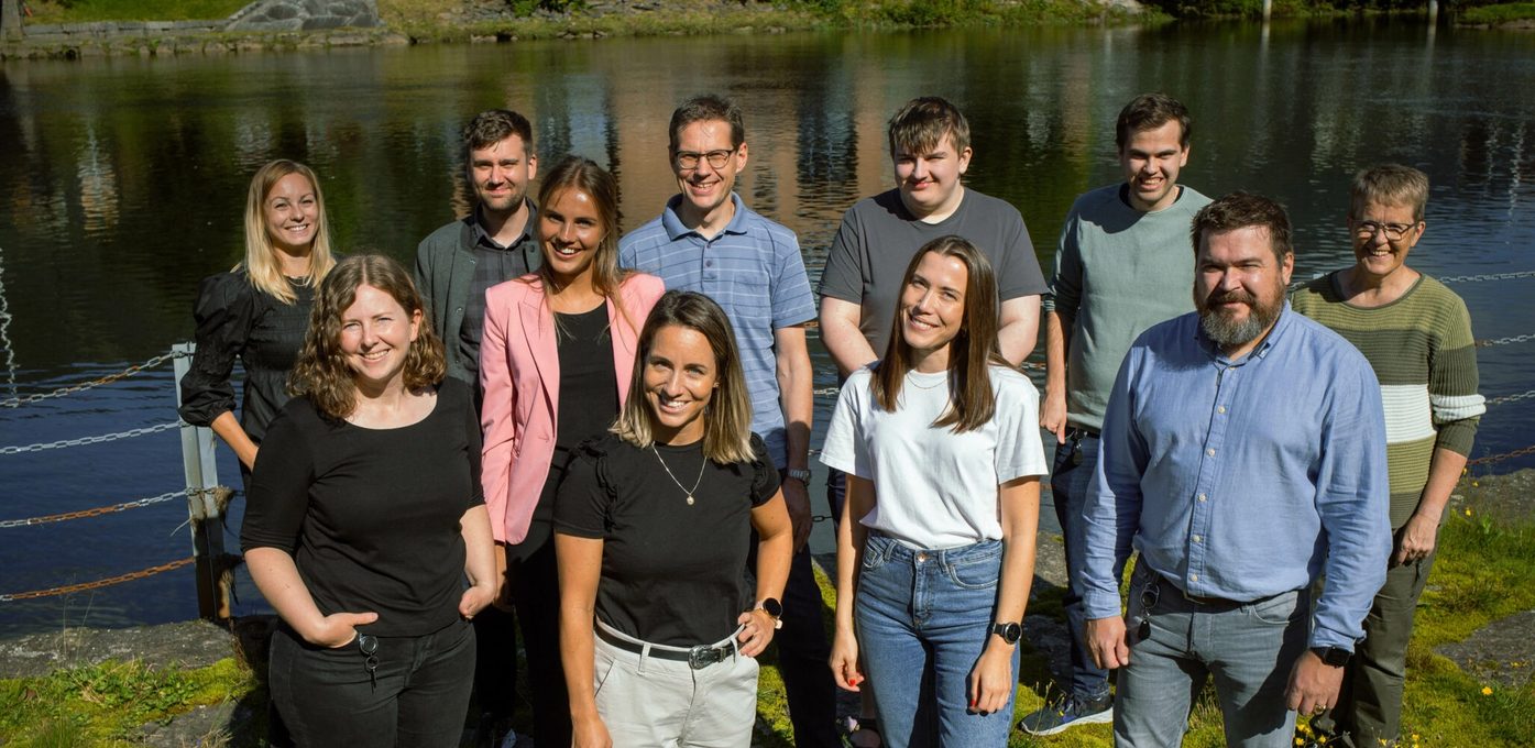 ti kollegaer smiler til kamera ved elvebredden i Førde.