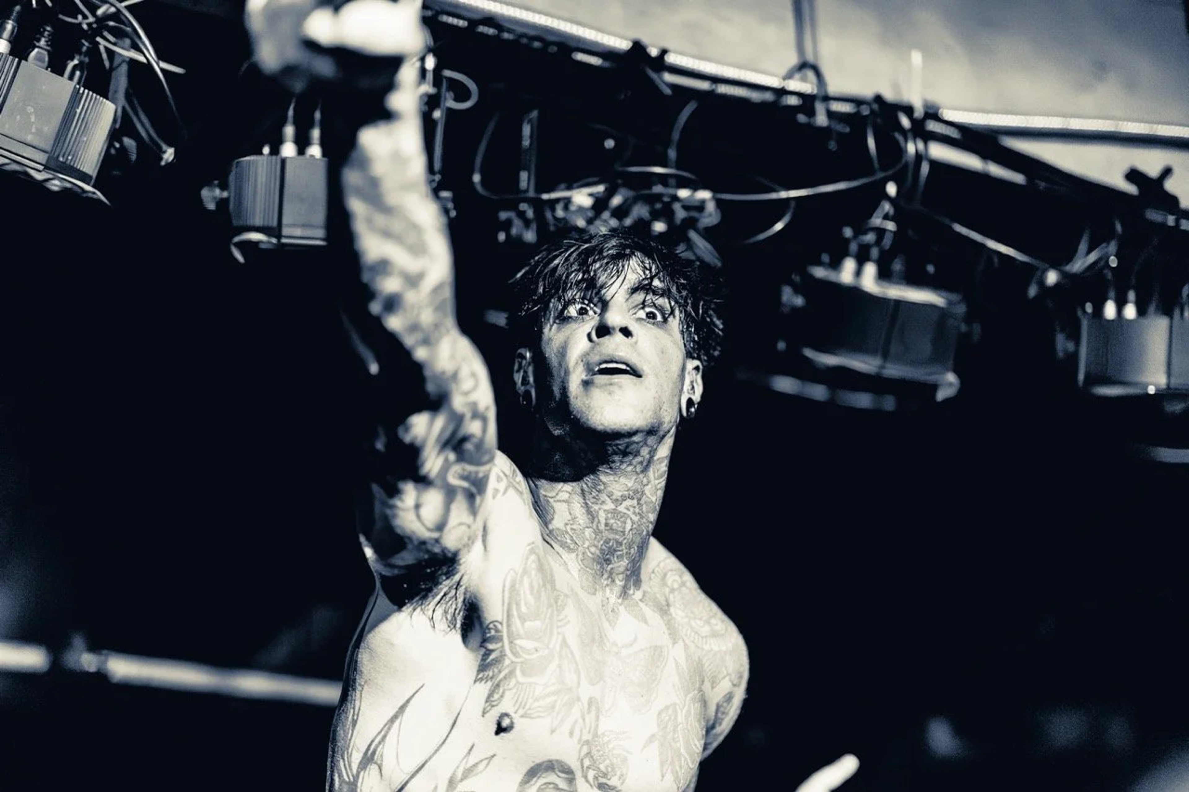 A shirtless tattooed male performer on stage looking upward, illuminated by overhead stage lighting rigs at Empire Live Underground.