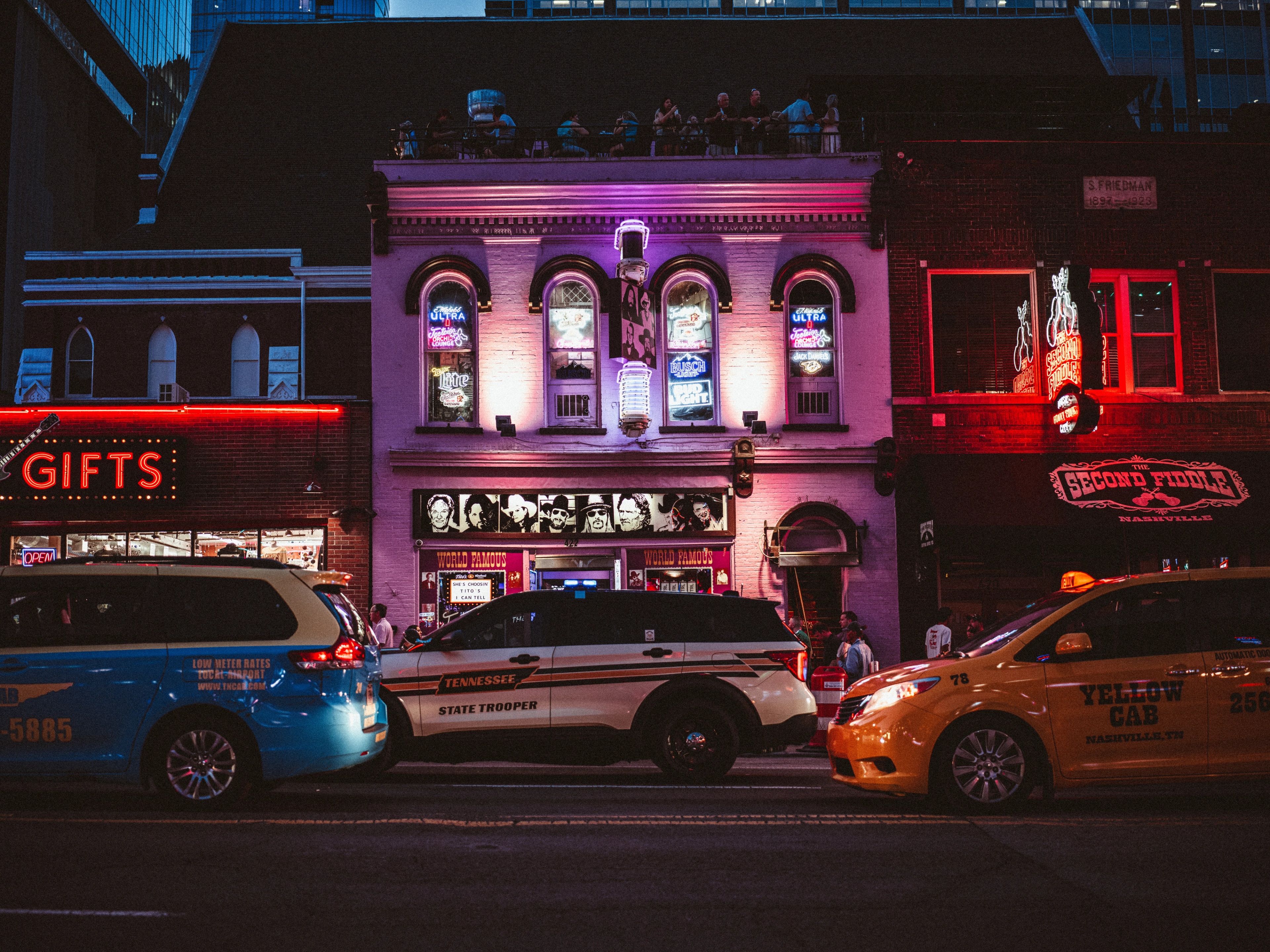 A neon-lit historic building facade in Nashville with police cars parked in front at night, red and purple stage lights illuminating the brick storefront.